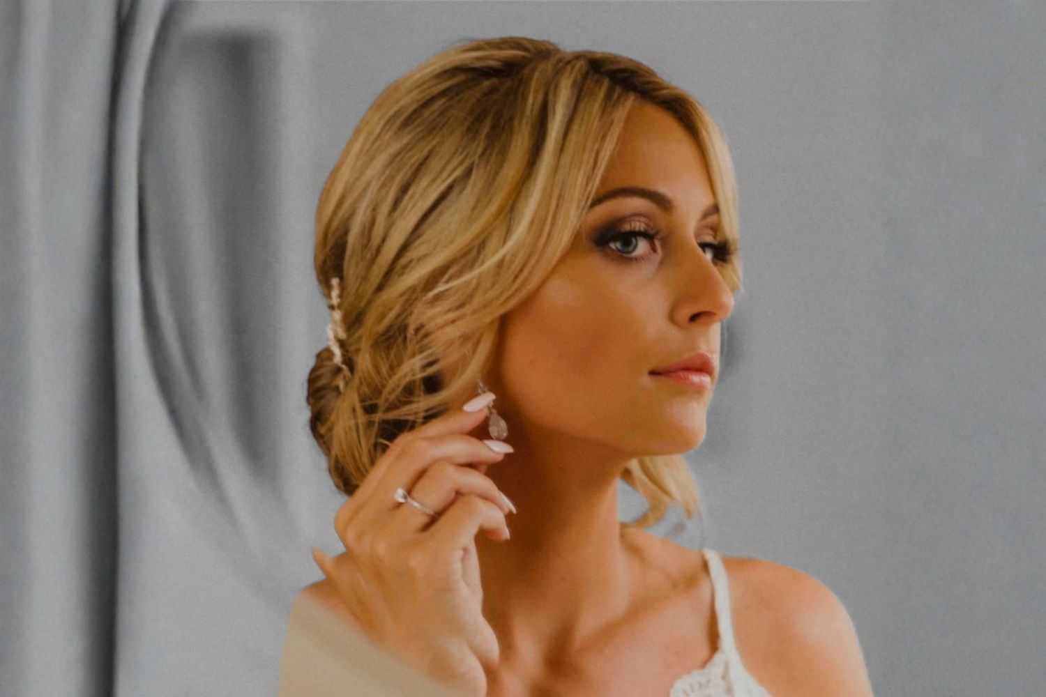 Woman with blonde hair looks sideways, adjusting earring in elegant setting.