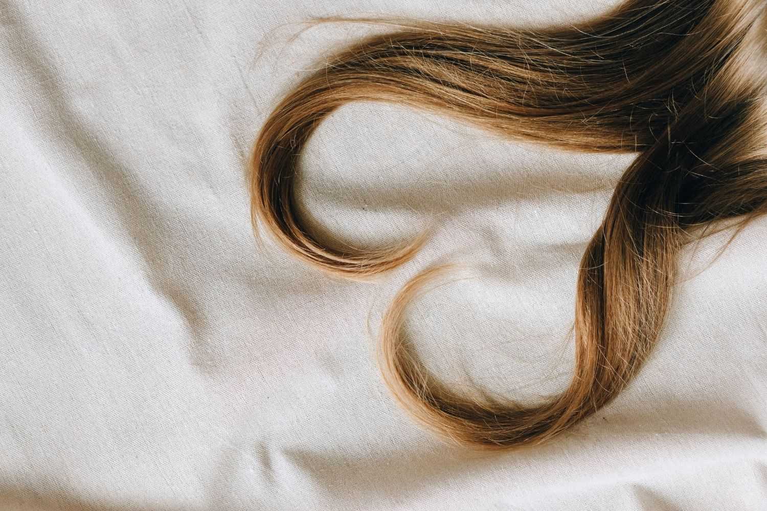 Long brown hair curls on a beige fabric background.