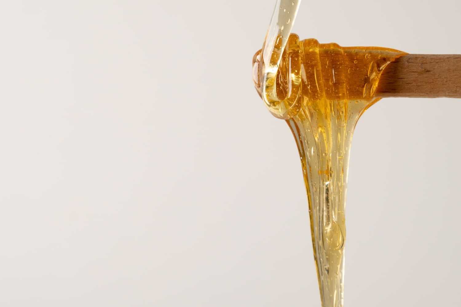 Honey dripping from a wooden stick against a plain background.
